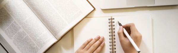 Top,View,Of,Student,Hand,Writing,A,Book,With,Laptop
